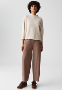 Lichtbeige, gestructureerde trui met een ronde hals, gecombineerd met bruine wijde broek met voorzakken en bruine sneakers.