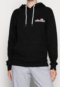 Černá mikina z bavlny s klokaní kapsou, bílými šňůrkami a vyšitým logem "ellesse" na hrudi. Hladké manžety a spodní lem.