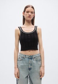 Juodas megztas trumpas viršus su tekstūruotu raštu, plačiu apvaliu kaklu ir kontrastingomis baltomis apdailomis. Derinamas su šviesiai skalbtais aukšto juosmens džinsais.