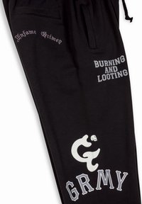 Zwarte trainingsbroek van katoen met decoratieve tekst. Bevat bedrukte zinnen "Infame Grimey," "BURNING AND LOOTING," en een gestileerd logo.