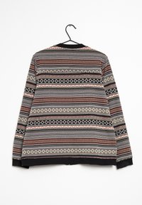Maglione a maglia con un motivo a fantasia in nero, rosso e crema. Presenta un colletto e dei polsini a coste; appeso a un gancio nero.