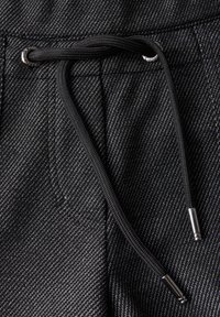 Pantalons noirs en tissu texturé avec une taille à cordon de serrage et des embouts en argent, présentant un motif diagonal subtil.