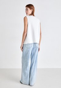 Hvit ribbestrikket ermeløs topp kombinert med lyseblå vid jeans, som viser en avslappet passform og minimalistisk design med myk tekstur.