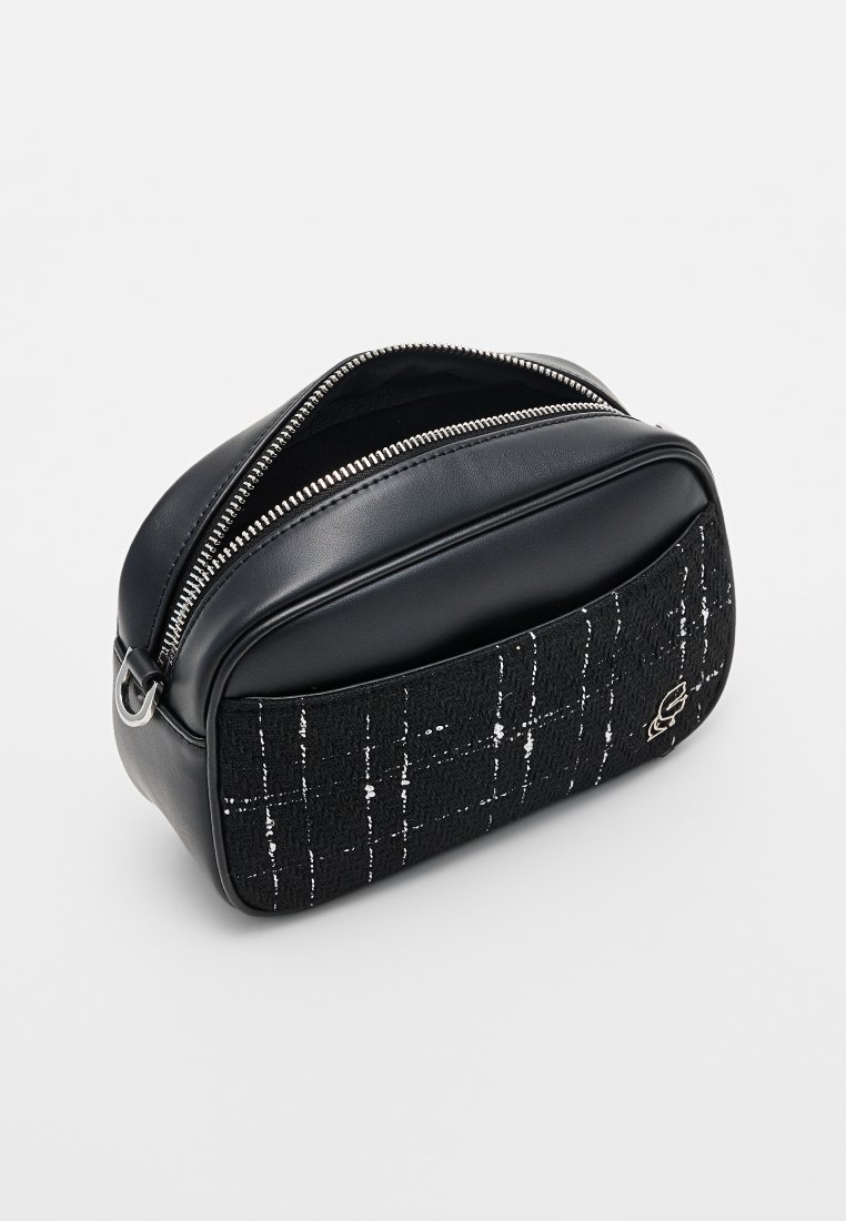Bolso negro con un diseño estructurado. Presenta una parte superior de cuero y un frente de tela negra texturizada con un patrón de cuadros blancos y una cremallera plateada.
