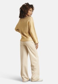 Gold ribbed sweater with a relaxed fit, paired with wide-leg beige trousers and white sneakers. Soft texture and casual design.
