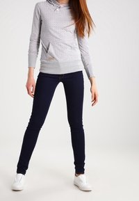 Grå huvtröja med multicolorerade prickar, med en känguruficka och ribbade muddar. Parat med mörkblå tajta jeans och vita sneakers.