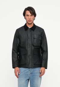 Black jacket made of textured material, featuring a corduroy collar, front snap buttons, one chest pocket, and two side pockets.