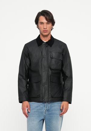Chaqueta negra hecha de material texturizado, con un collar de pana, botones a presión en el frente, un bolsillo en el pecho y dos bolsillos laterales.