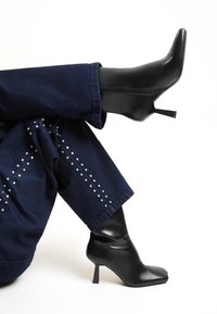 Botine negre cu toc, cu vârf ascuțit și un design șifonat în partea superioară. Fabricate din material neted, asortate cu blugi tă dark cu tinte argintii.