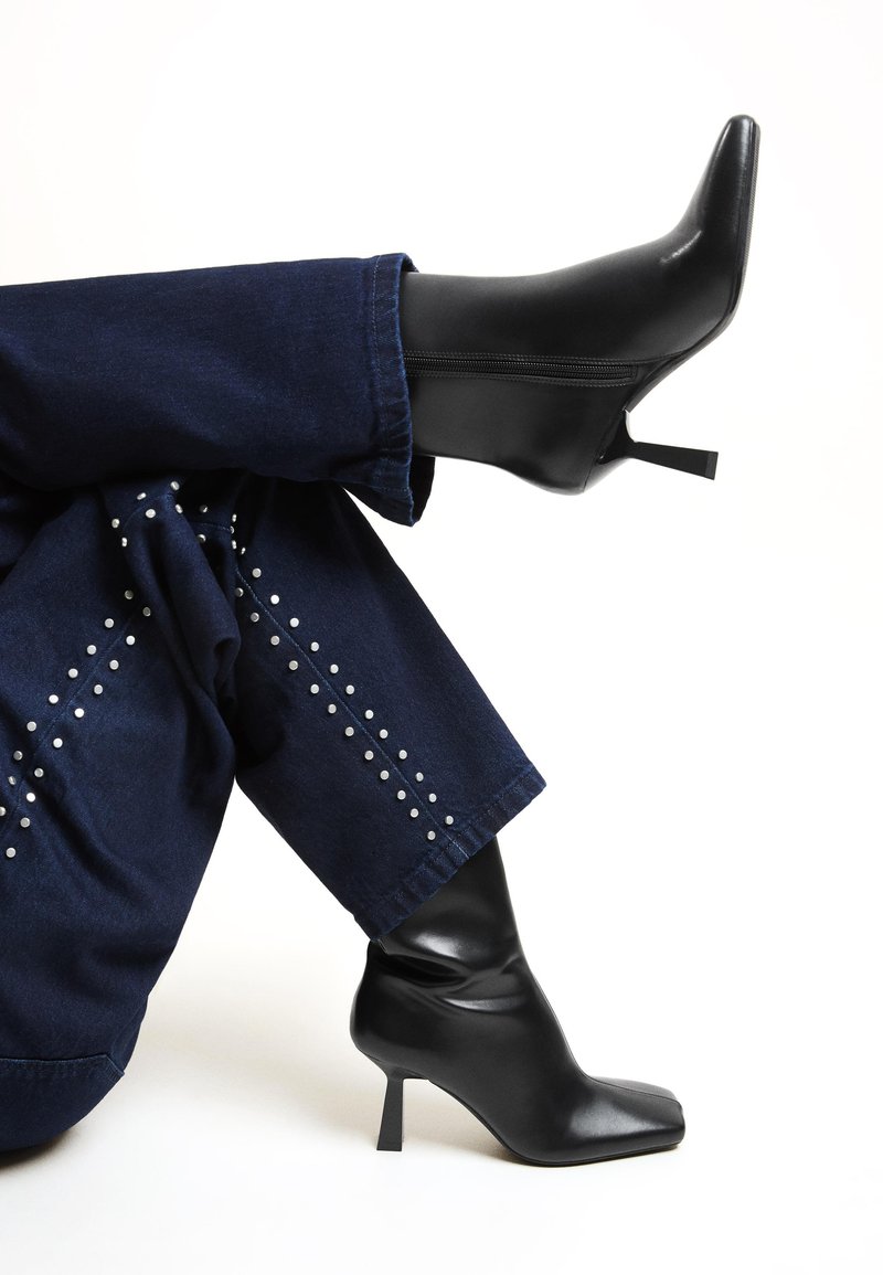 Botine negre cu toc, cu vârf ascuțit și un design șifonat în partea superioară. Fabricate din material neted, asortate cu blugi tă dark cu tinte argintii.