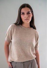 Beige katoenen trui met korte mouwen en een ronde hals, zacht van textuur en met geribbelde manchetten, gecombineerd met lichtgrijze pantalon met een knoopdetail.