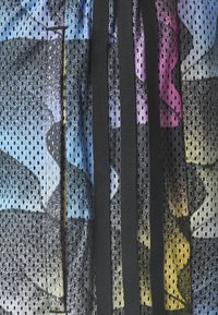 Tessuto a rete con motivi astratti neri e colorati; presenta tre strisce verticali nere; texture leggera e traspirante.