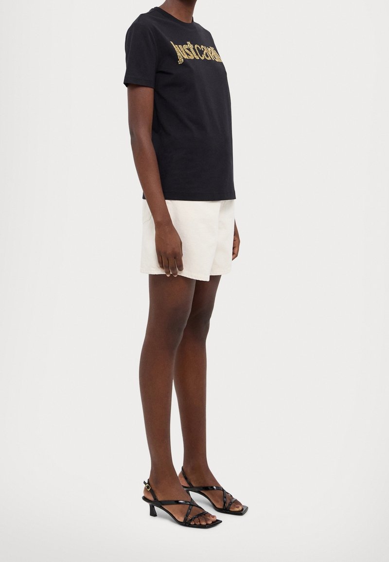 Czarna bawełniana koszulka z złotym napisem "justcause", w połączeniu z białymi szortami i czarnymi sandałami na paski. Design jest luźny i dopasowany.