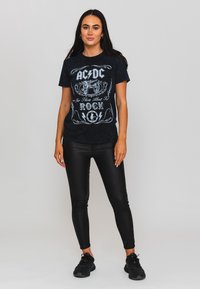 Black cotton AC/DC graphic t-shirt featuring white text and lightning bolt designs, paired with black fitted pants and black sneakers.