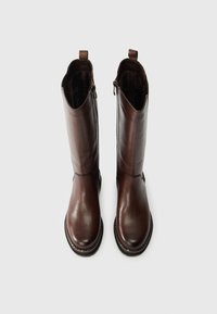 Ζευγάρι ψηλών, σκούρων καφέ δερμάτινων μπότες με πλαϊνούς φερμουάρ και λωρίδες πρόσδεσης, όρθιες σε άσπρο φόντο.