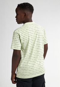 Camiseta de algodón verde claro con mangas cortas, que presenta rayas horizontales negras. La tela tiene una textura suave y un cuello redondo.
