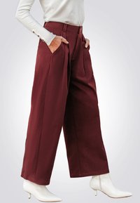 Bordeaux wijde broek gemaakt van textiel met voorzakken, gecombineerd met witte puntige enkelboots.