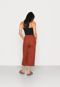 Pantalons larges couleur rouille en tissu doux, dotés d'une taille élastique. Associés à un top sans manches noir et des sandales à imprimé animal.