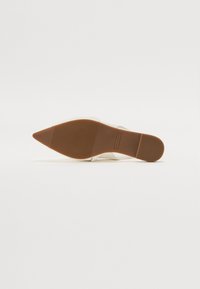 White pointed-toe heeled shoe with a smooth leather upper and a textured brown rubber sole. Minimalist design, no visible hardware or patterns.