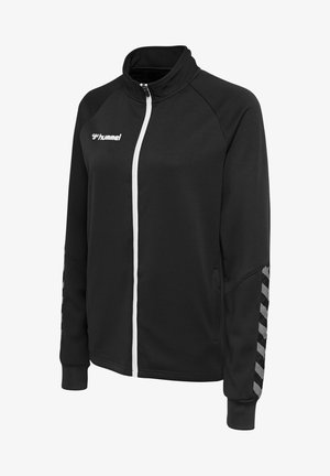 Sort zip-jacket med høj krave, struktureret stof og hvid lynlås. Har mønstrede striber på ærmerne og et logo på brystet.