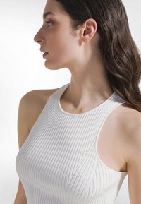 Biały prążkowany top na ramiączkach z wysokim dekoltem, bez rękawów, wykonany z teksturowanej tkaniny z delikatnymi liniami i detalami szwów.