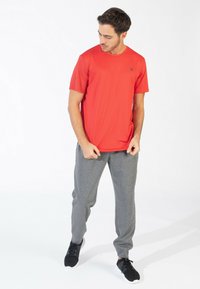 Rood sportshirt met korte mouwen en een ronde hals, gecombineerd met grijze textuur joggingbroek en zwarte sportschoenen op een effen achtergrond.