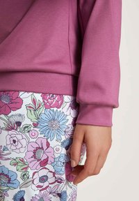 Paarse langemouwtop met een relaxte pasvorm, gecombineerd met witte onderkleding met een multikleurig bloemenpatroon. Zachte stof, zichtbare stiksels.