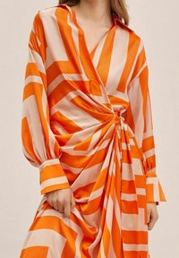 Vestido largo de manga larga con un patrón en zigzag naranja y rosa claro, elaborado con una tela suave y con un detalle fruncido en la cintura.