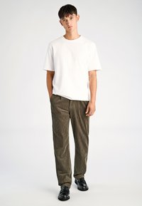 Wit T-shirt met korte mouwen, olijfgroene corduroy broek met verticale strepen en zwarte schoenen. Eenvoudig ontwerp, reguliere pasvorm, casual stijl.