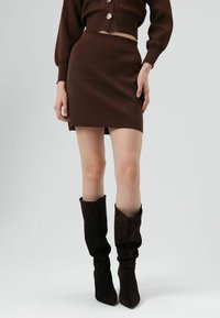 Bruine geribbelde mini-rok gecombineerd met bruine suède laarzen tot aan de knie met een nonchalante pasvorm. De outfit heeft een aansluitende silhouet en een gladde textuur.