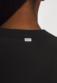 T-shirt noir avec col rond et ourlet cousu, affichant une petite étiquette blanche avec "PUMA" au niveau du cou. Texture douce.