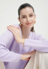 Lavendelfarbenes Strickpullover mit V-Ausschnitt, gerippten Bündchen, getragen mit cremefarbenen Hosen. Verfügt über eine glatte Textur und einen minimalistischen Stil.