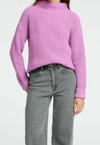 Pull rose tricoté à col montant et texture côtelée, associé à un jean gris taille haute avec une ceinture en accent.