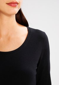 Czarna bluzka z długim rękawem i okrągłym dekoltem. Tkanina wydaje się miękka i lekko elastyczna, o gładkiej teksturze i bez widocznych wzorów.