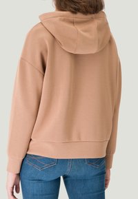Loszittende, zachte beige hoodie met een capuchon met trekkoord, lange mouwen en geribbelde boorden, gecombineerd met blauwe denim jeans.