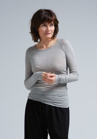 Langärmliges graues T-Shirt aus weichem Stoff, mit rundem Halsausschnitt und figurbetonendem Design, kombiniert mit lockeren schwarzen Hosen.
