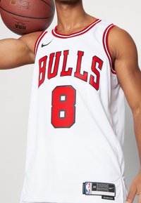 Maglia da basket bianca con dettagli rossi, con la scritta "BULLS" e il numero "8" bordato di nero. Realizzata in materiale retato traspirante. Etichetta del logo NBA visibile.