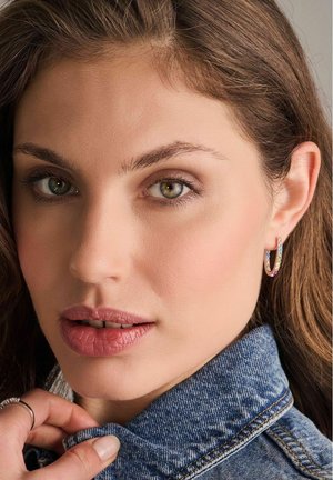 Guld hoops øreringe med multikolore stenakcenter, båret af en model med langt brunt hår og en denimbeskytter, der fremhæver ansigtstræk.