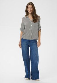 Black and white striped button-up shirt with rolled sleeves, paired with wide-leg blue denim jeans, standing on a neutral background.