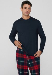 Námořnická dlouhá košile v kombinaci s pyžamovými kalhotami v červené a zelené kárované vzoru. Měkká tkanina, uvolněný střih a elastický pas s detailem na šňůrku.