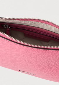 Różowa torebka ze skóry ziarnistej z zamkiem błyskawicznym w kolorze srebrnym, wyposażona w gładką podszewkę i metkę z logo marki wewnątrz.
