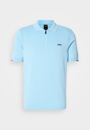 Lys blå polo skjorte laget av strikket stoff, med glidelåskrage, korte ermer og en liten svart logo på brystet.