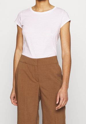 Woman wearing a light pink and white striped short-sleeve shirt tucked into high-waisted brown pants against a plain background.