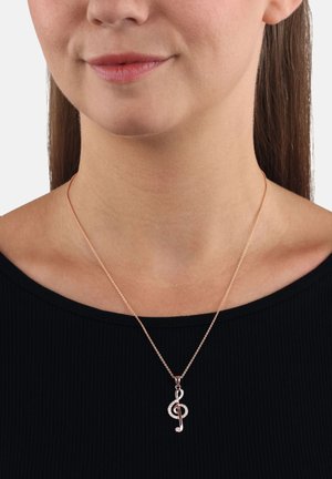 Collana in oro rosa con un pendente a forma di nota musicale, caratterizzata da una superficie liscia e decorazioni incastonate, indossata sopra una maglietta nera.