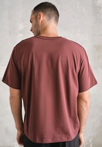 Bordowa koszulka z miękkiej bawełny, o luźnym kroju, z krótkimi rękawami i zaokrąglonym dołem. Minimalistyczny design, brak widocznych logo.