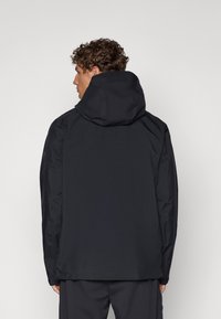 Veste imperméable noire avec capuche, texture douce, coupe standard et design minimaliste. Les caractéristiques comprennent des manches longues et un ourlet droit.