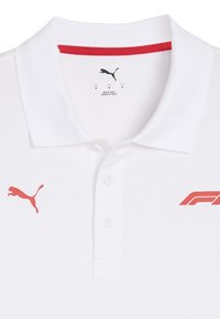 Biała koszulka polo z czerwoną lamówką przy kołnierzyku, z czerwonym logo Puma na lewej piersi oraz grafiką F1 po prawej stronie.