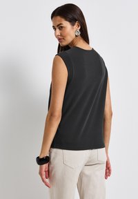Top nero senza maniche con scollatura rotonda, texture liscia, abbinato a pantaloni crema. Nota bracciale nero come accessorio al polso.