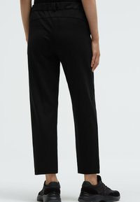 Black trousers made from a smooth fabric, featuring a high waistband and a relaxed, straight-leg design, paired with black sneakers.