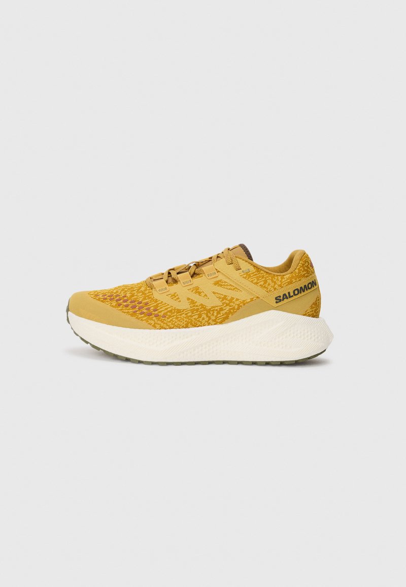 Scarpa sportiva gialla con tomaia texturizzata, punta rinforzata e suola in schiuma leggera. Presenta un sistema di allacciatura e il marchio 'Salomon' sul tallone.